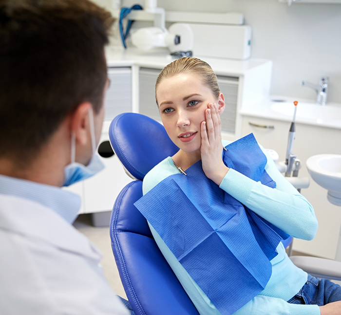 Young woman holding her face in pain while talking to oral surgeon about facial trauma treatment