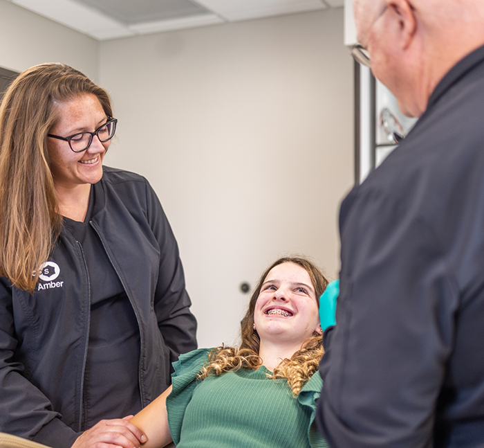 Young woman with braces smiling at two oral surgery team members in Lancaster