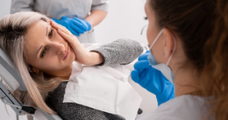 Woman holding her jaw in pain while talking to her dentist