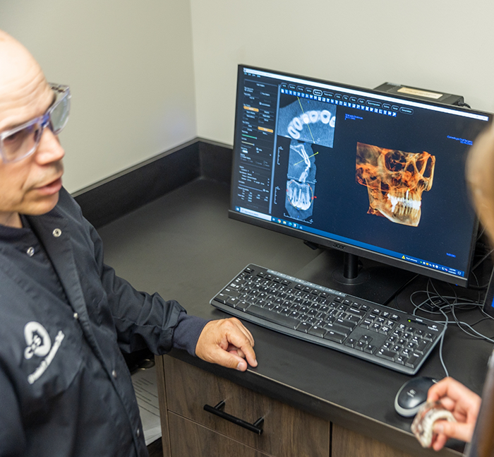 Oral surgeon sitting at desk with computer showing digital models of a patients teeth and jaws